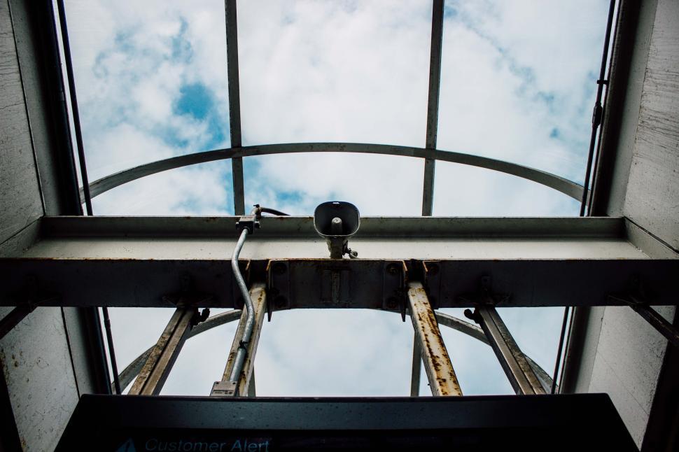 Free Image of View of an industrial ceiling structure with a speaker and clouds above 