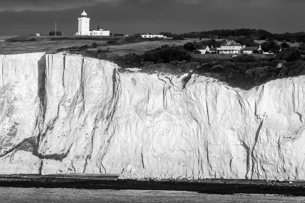 Free Image of Cliffs rise above lighthouse and quaint village by the sea 