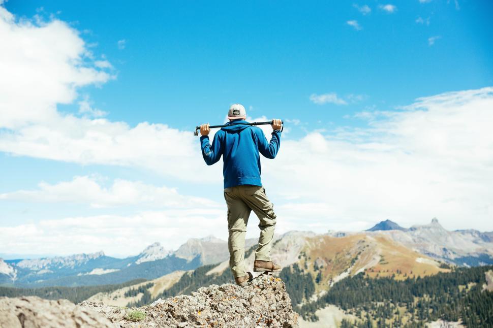 Free Image of Hiker stands on a mountain peak with a backpack and staff enjoying the view 