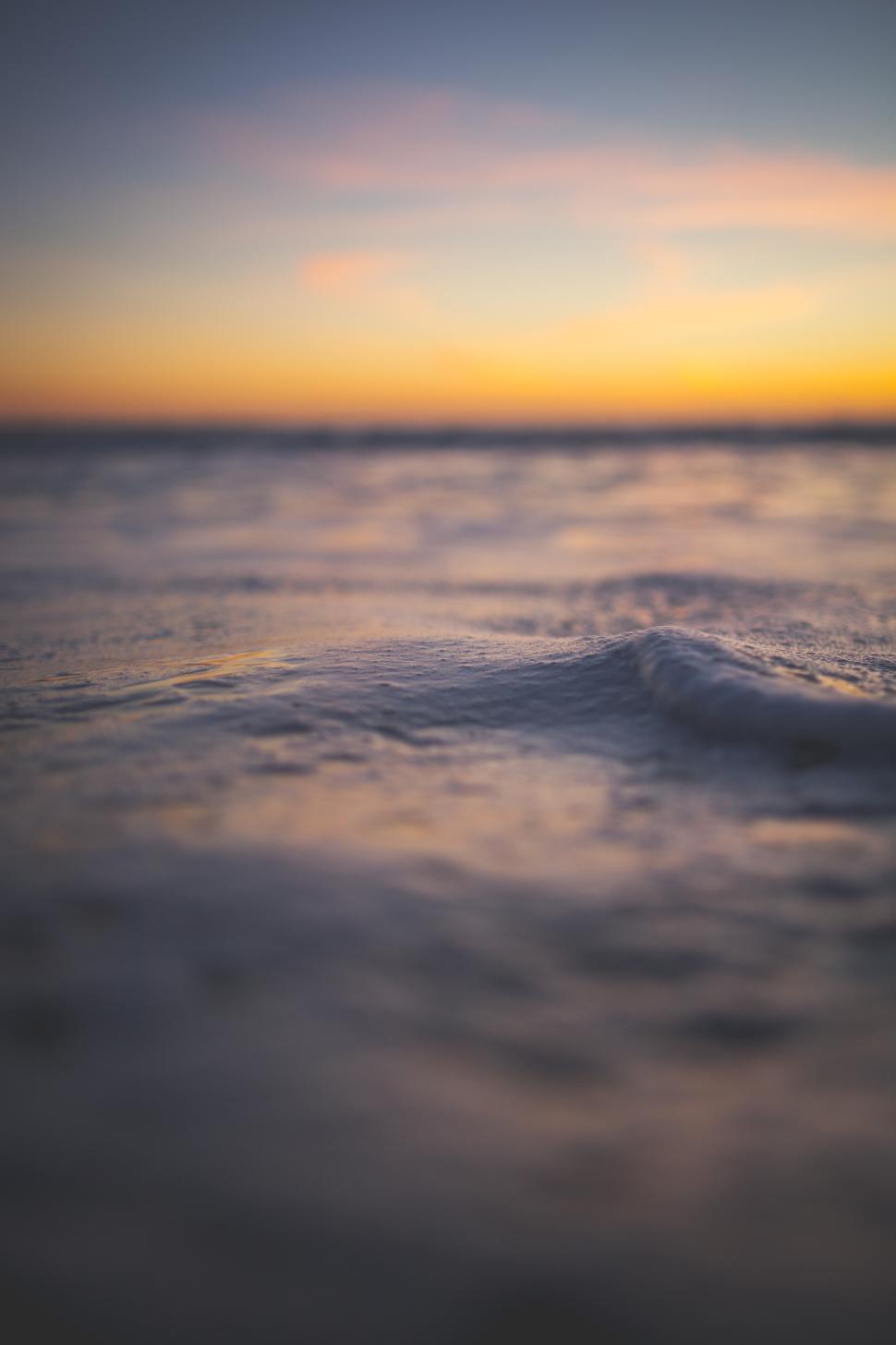 Free Image of Calm waves gently rolling on the shore during a vibrant sunset 