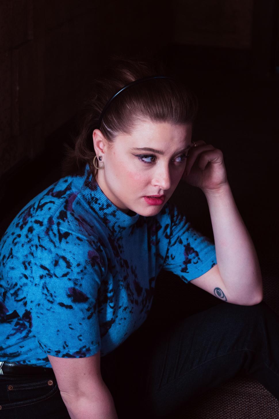 Free Image of Young woman in blue outfit thoughtfully sitting in dark urban setting 