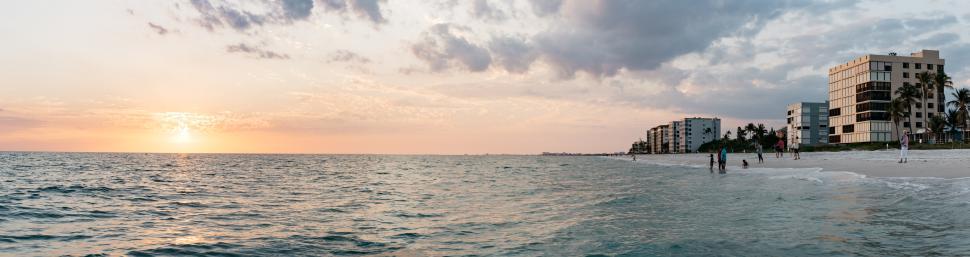 Free Image of Sunset over a calm beach with distant buildings in view 