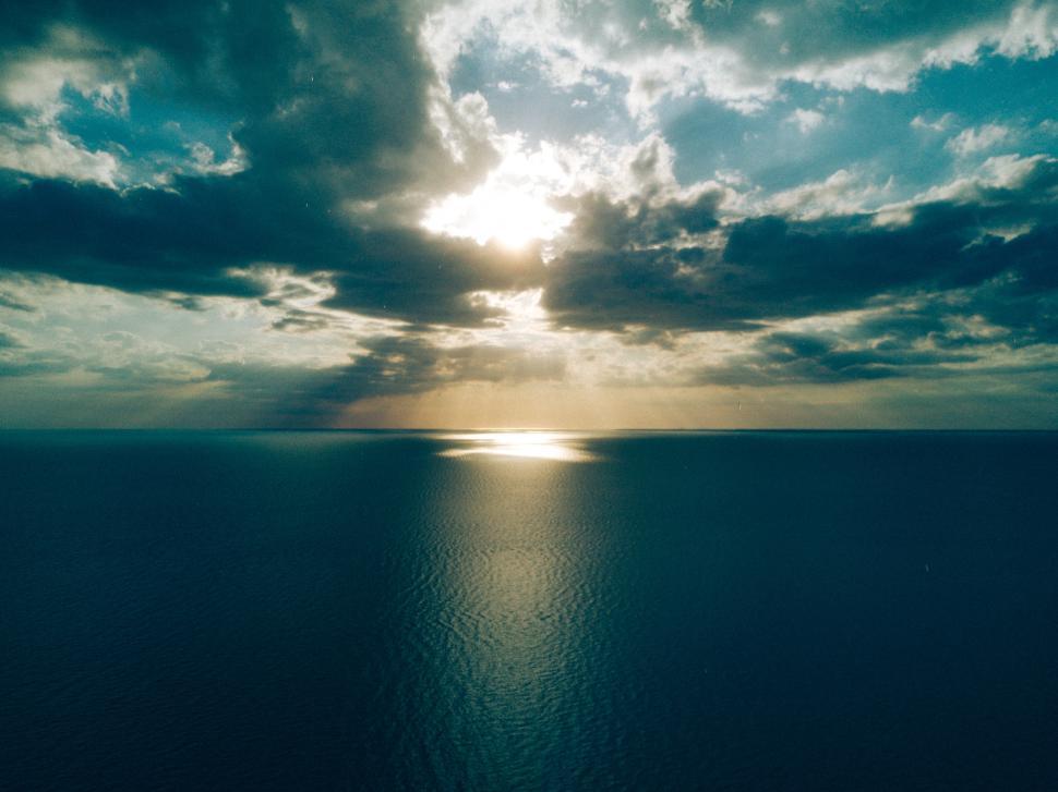 Free Image of Sunlight breaking through clouds over calm ocean waters 