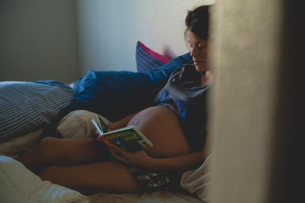 Free Image of Expecting mother reading a bedtime story in a cozy bedroom sanctuary 