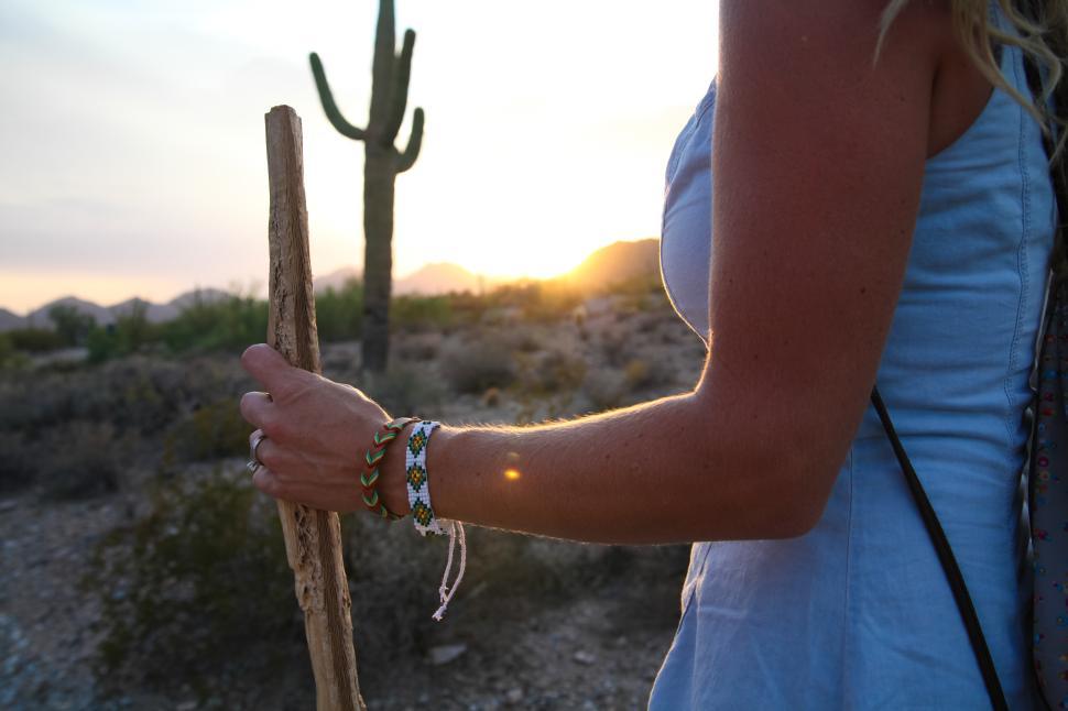 Free Image of Woman hiking with a stick in the desert at sunset near cacti 