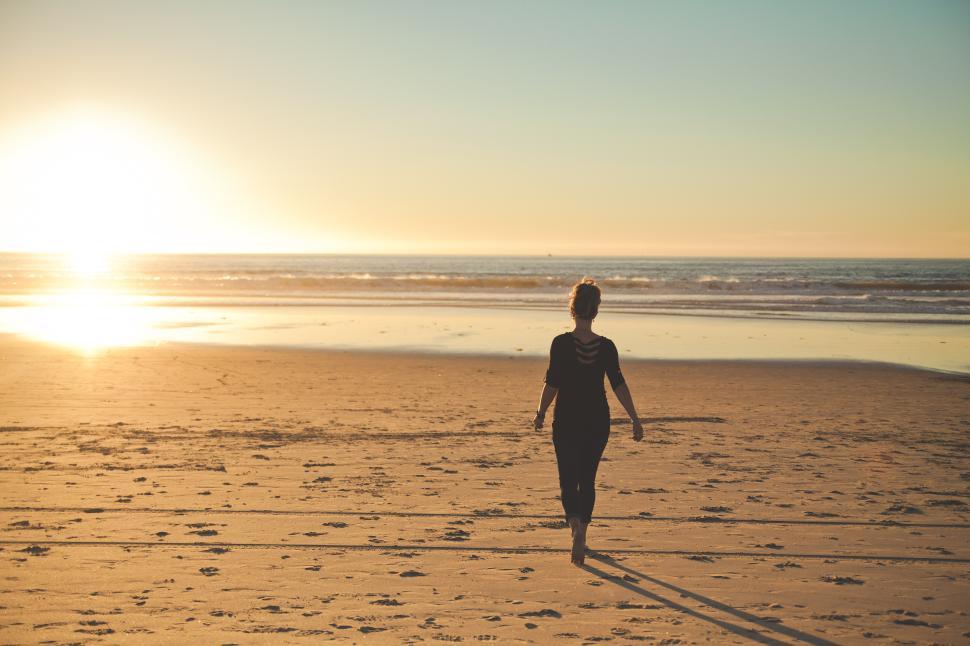 Free Image of Woman walks along a sandy beach at sunset near the ocean waves 
