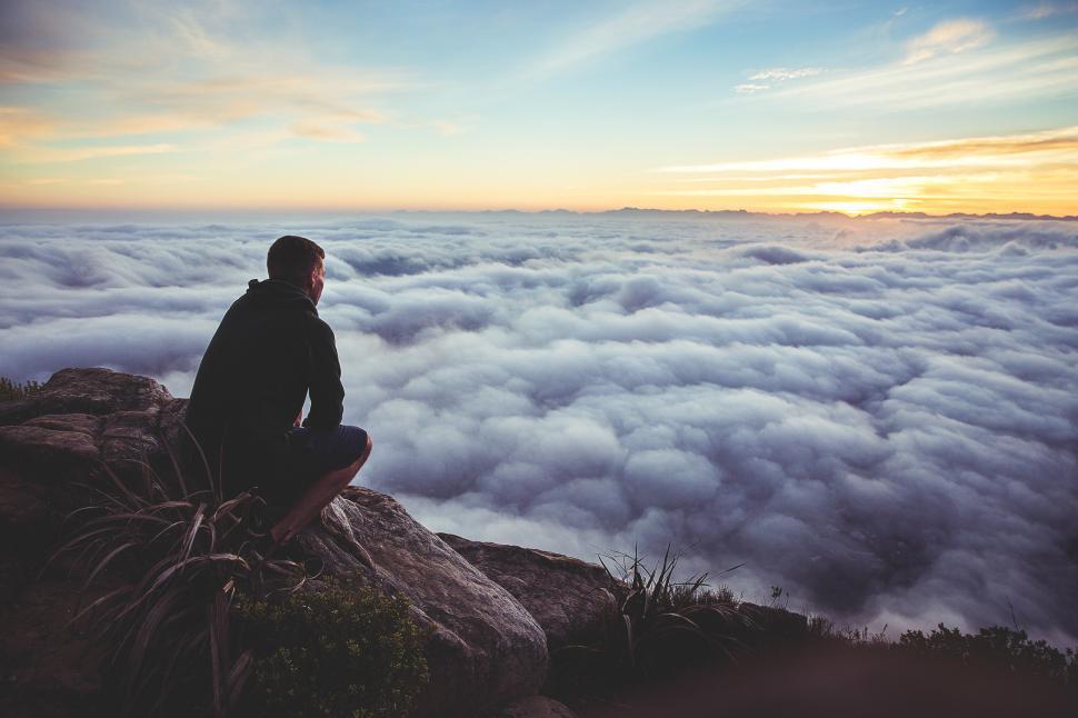 Free Image of Man gazing over clouds at sunset from mountain peak 