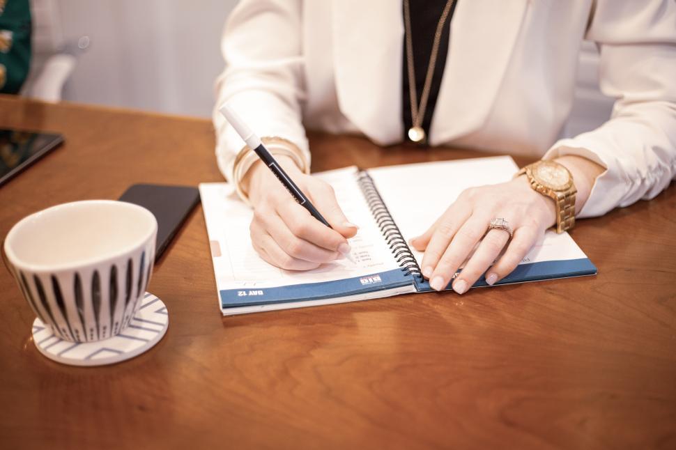 Free Image of Woman writing in planner during meeting at a wooden table 
