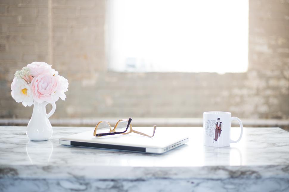 Free Image of Workspace with flowers, glasses, and mug on marble table 
