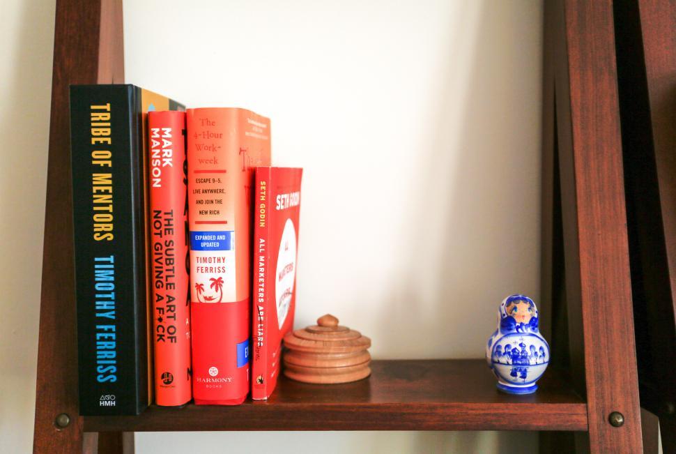 Free Image of Books on a wooden shelf displaying diverse topics and decorative items 