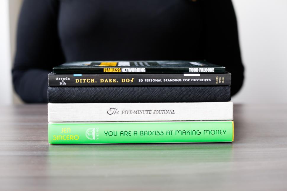 Free Image of Books on personal development stacked on a table with a person in the background 