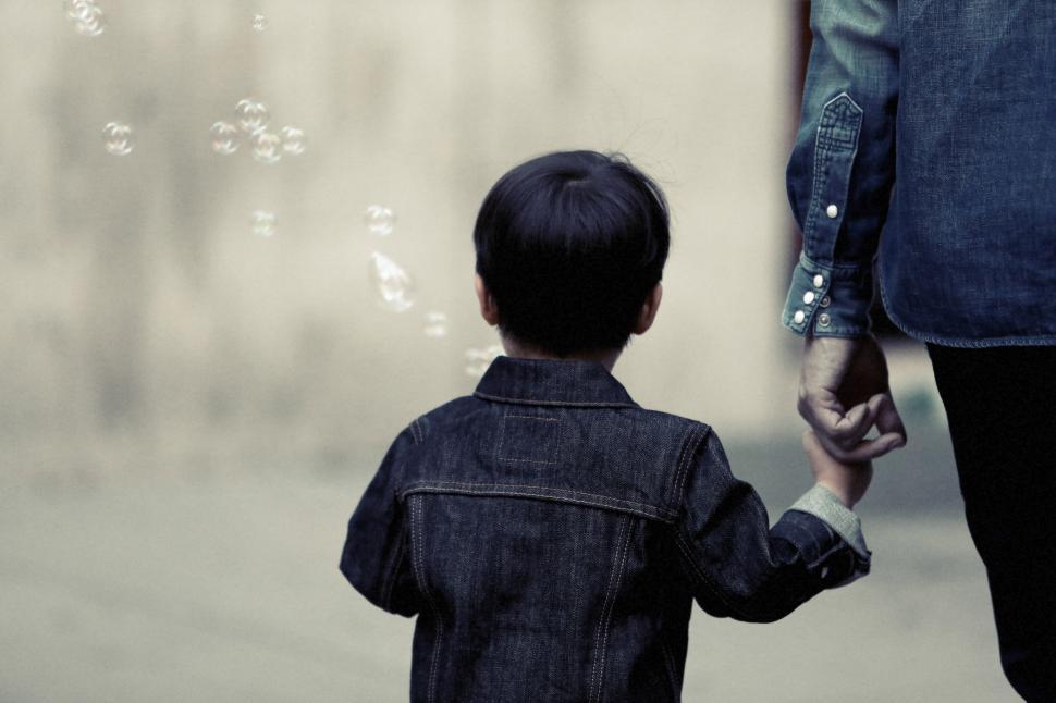 Free Image of Child holding adult s hand while walking towards bubbles outdoors 