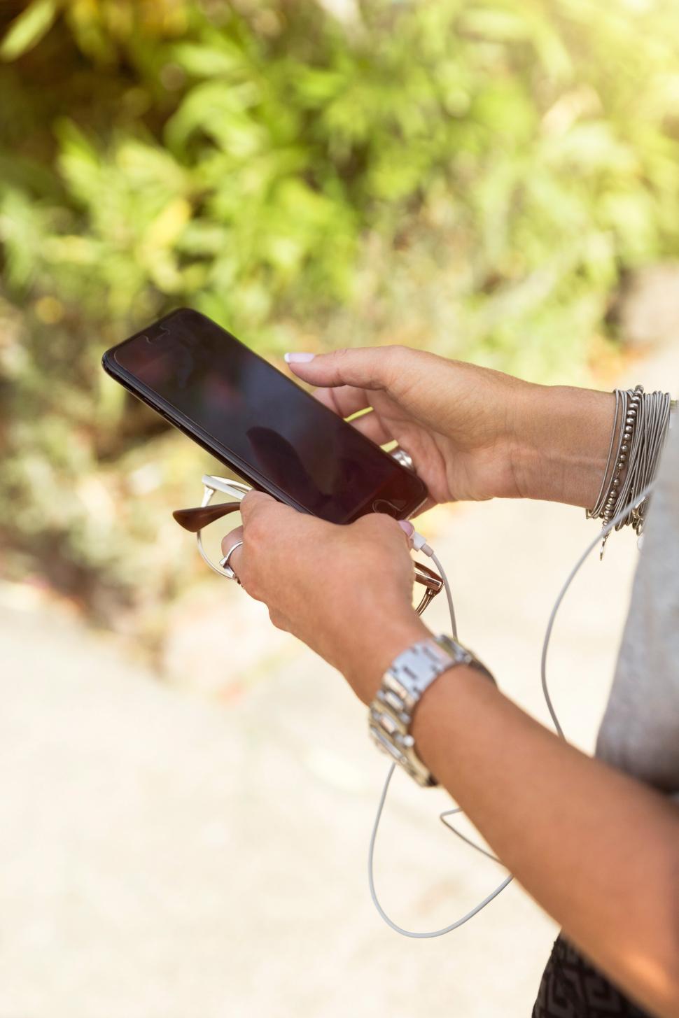 Free Image of Person using smartphone while holding sunglasses in park 
