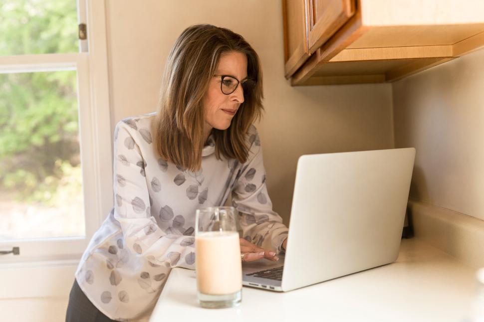 Free Image of Woman working on laptop at kitchen counter during daytime 
