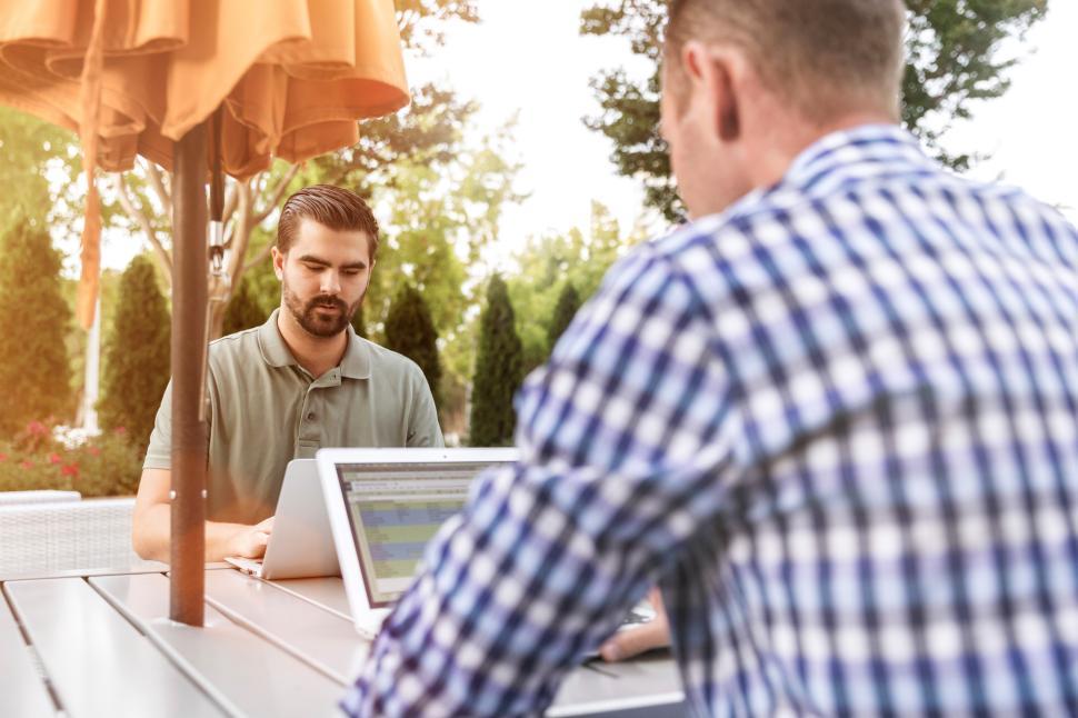 Free Image of Two men working outdoors on laptops in a sunny garden 