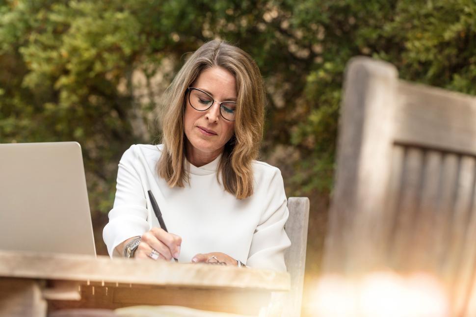Free Image of Woman writing outdoors while working on laptop in nature 