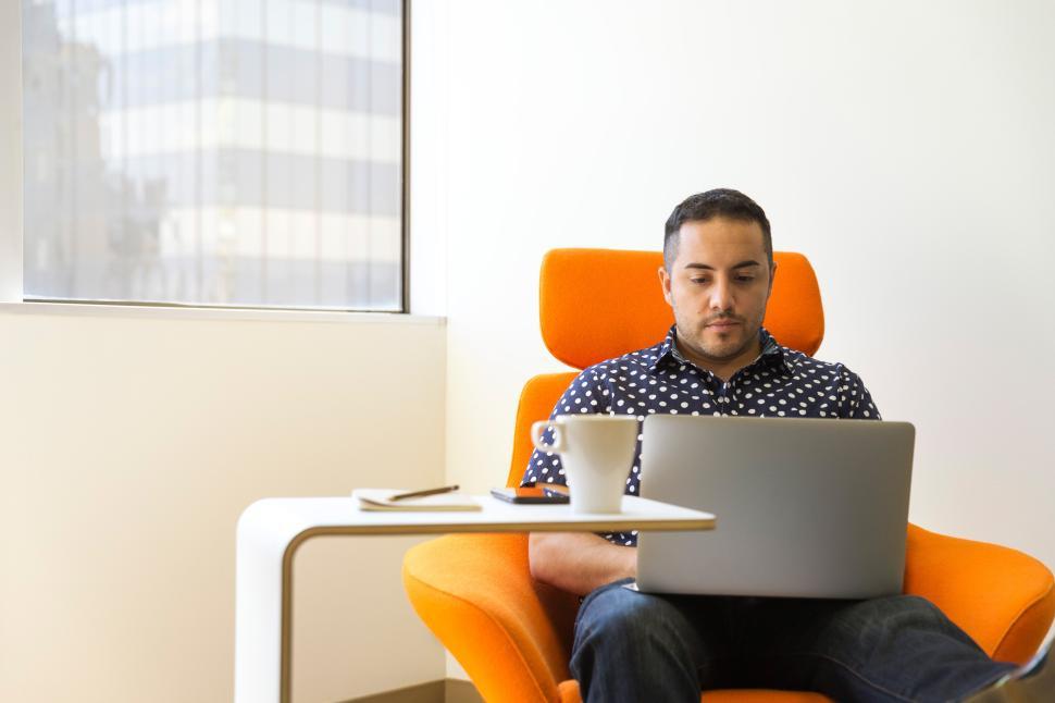Free Image of Young man working on laptop in an orange armchair 