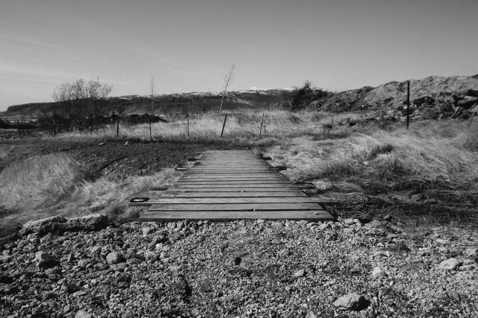 Free Image of Wooden pathway through open landscape in black and white 