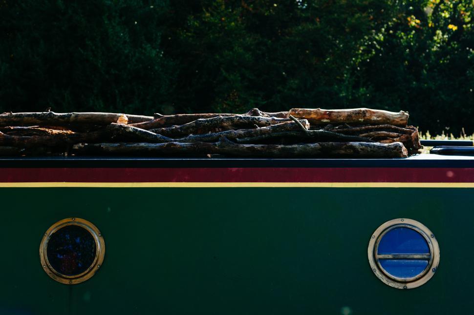 Free Image of Logs resting on a colorful narrowboat in nature 