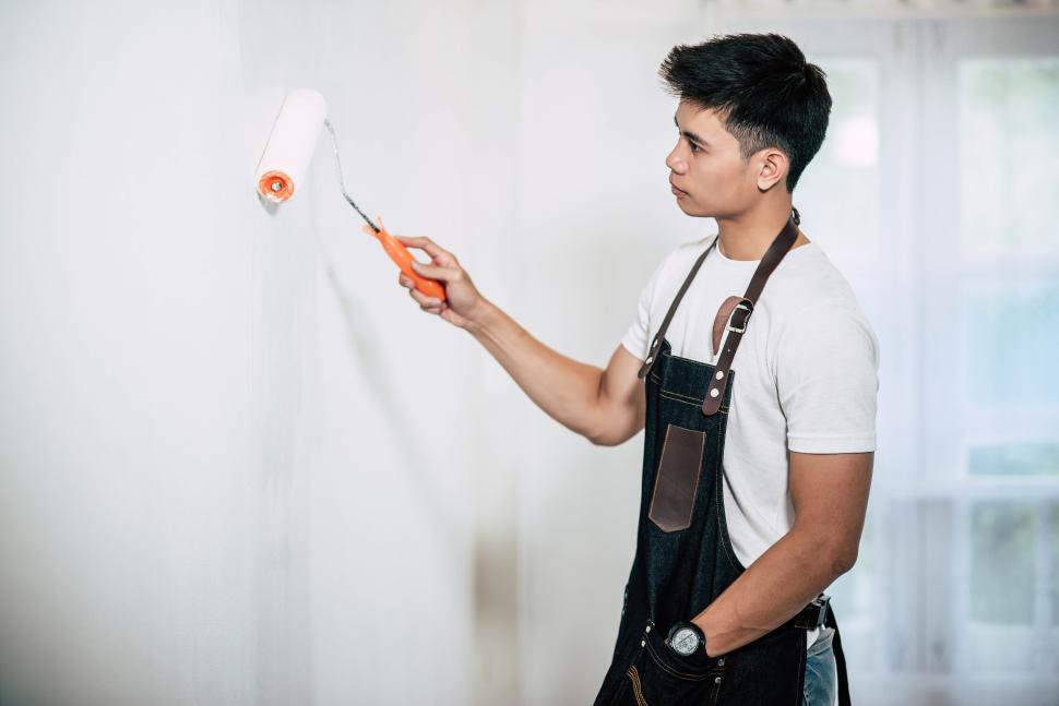 Free Image of A carpenter holds a paintbrush and paints wood. 
