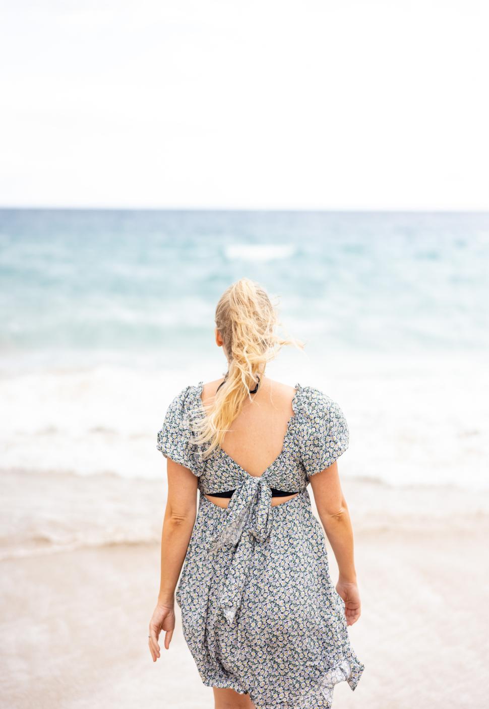 Free Image of Woman walking towards the ocean on a breezy beach day 