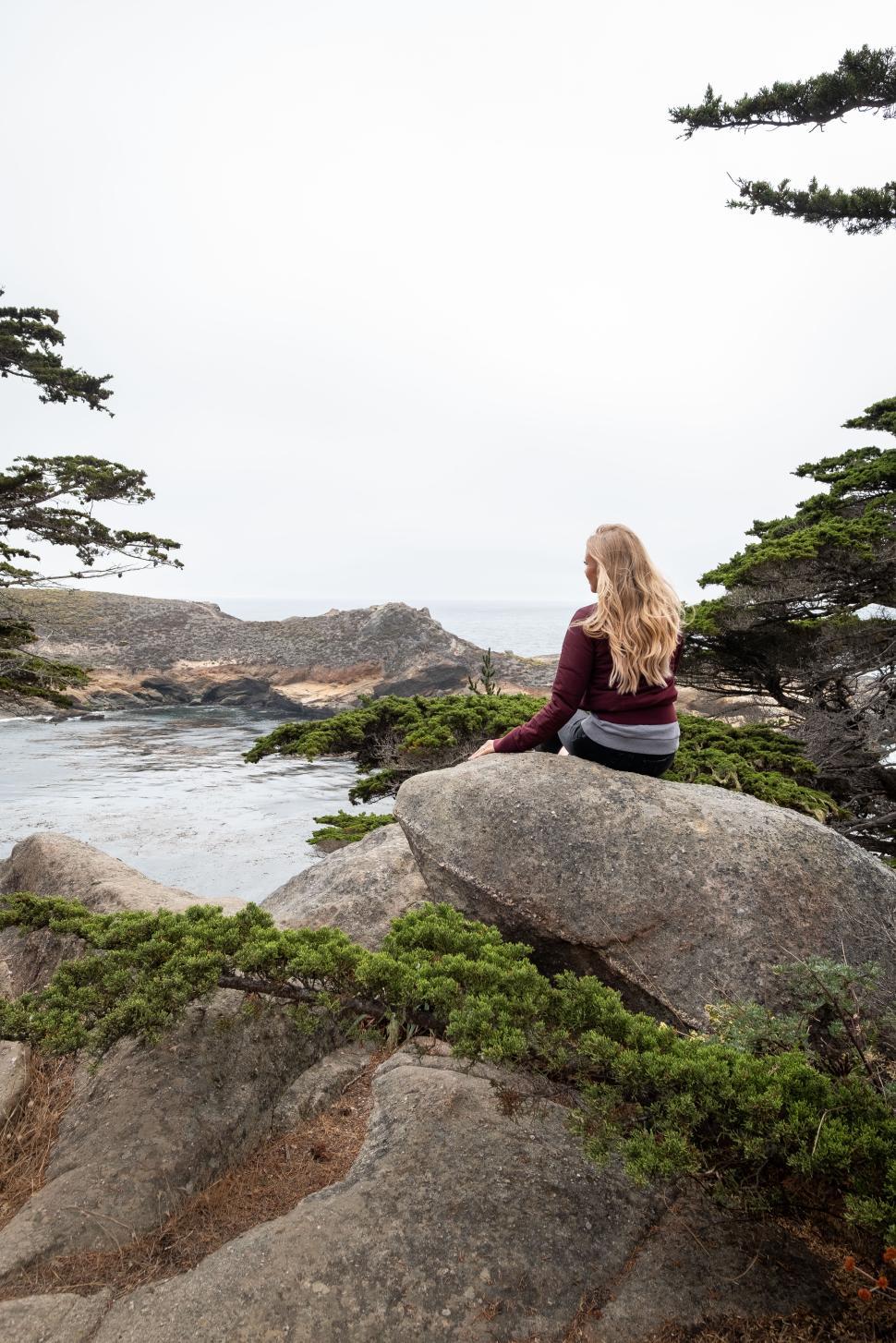 Free Image of Scenic coastal view with a woman enjoying nature on a rock 