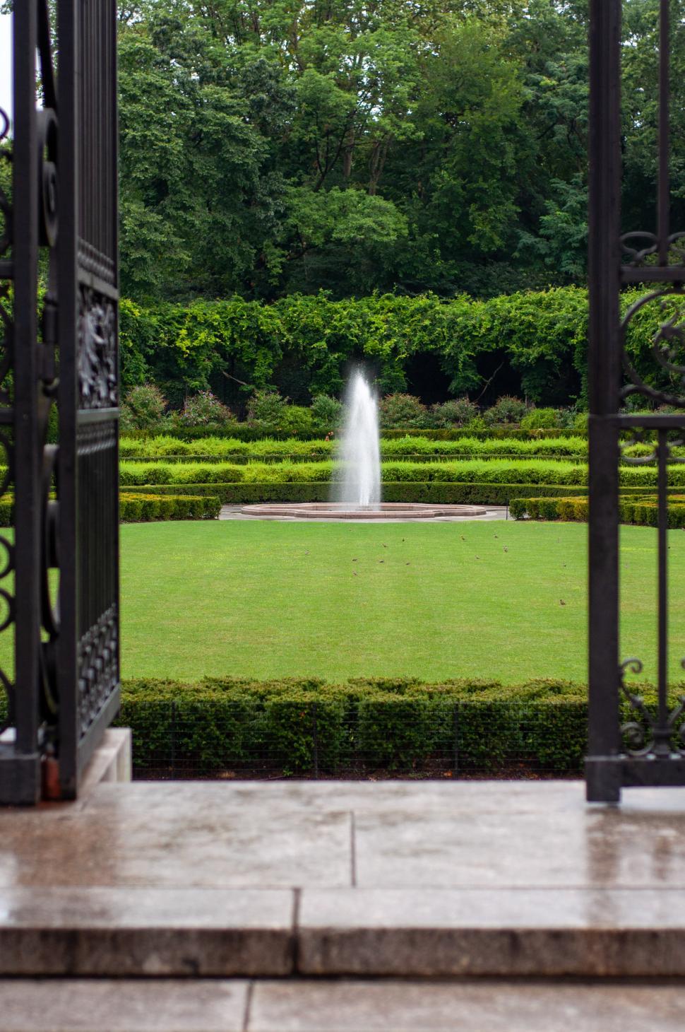 Free Image of Beautiful garden fountain viewed from ornate iron gate entrance 