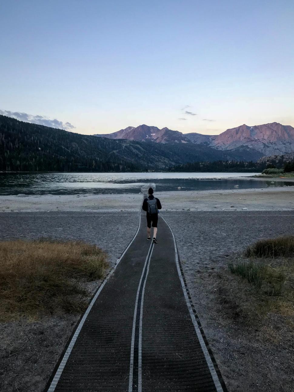 Free Image of Person walking on a boardwalk by a serene lake at dusk 