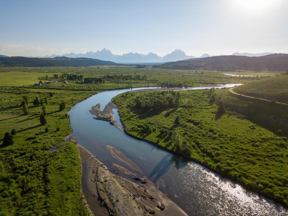 Free Image of Serene river winding through lush green valley at sunset 
