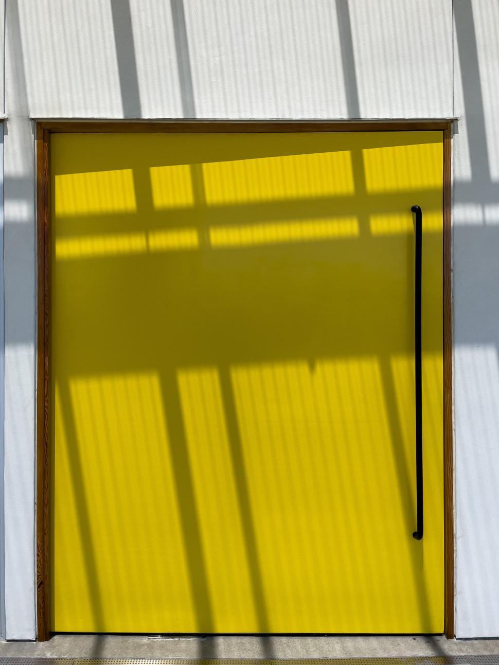 Free Image of Bright yellow door with shadows cast from nearby structures during midday 