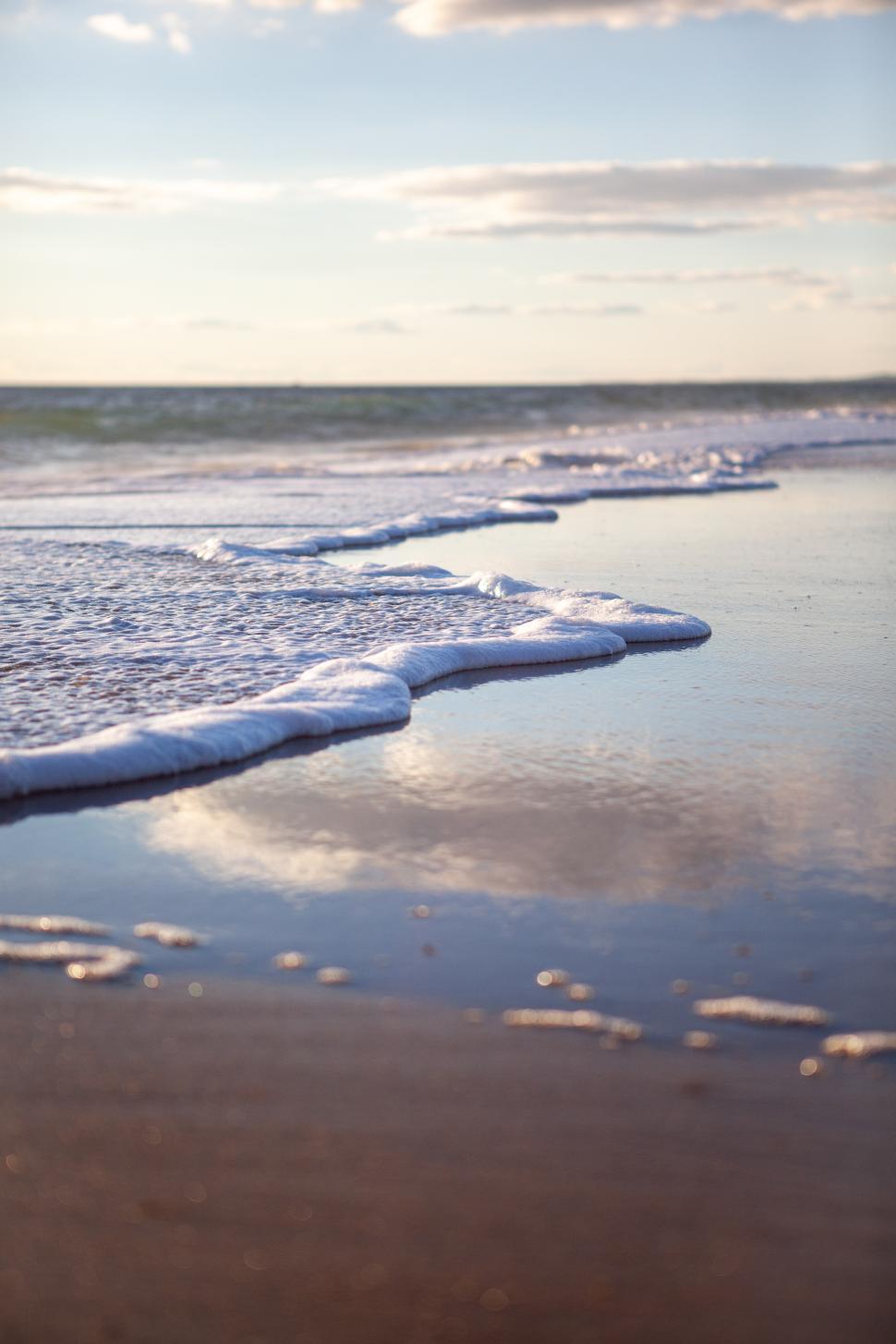 Free Image of Waves gently lap at the shoreline during sunset near the ocean 
