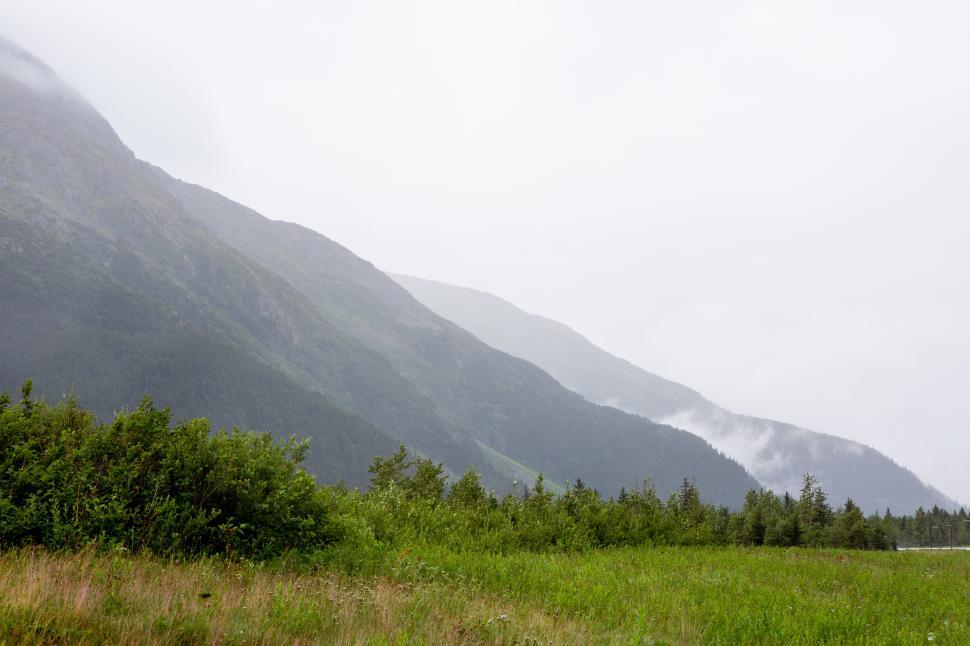 Free Image of Mountains and mist cover the green valley beneath the cloudy sky in Alaska 