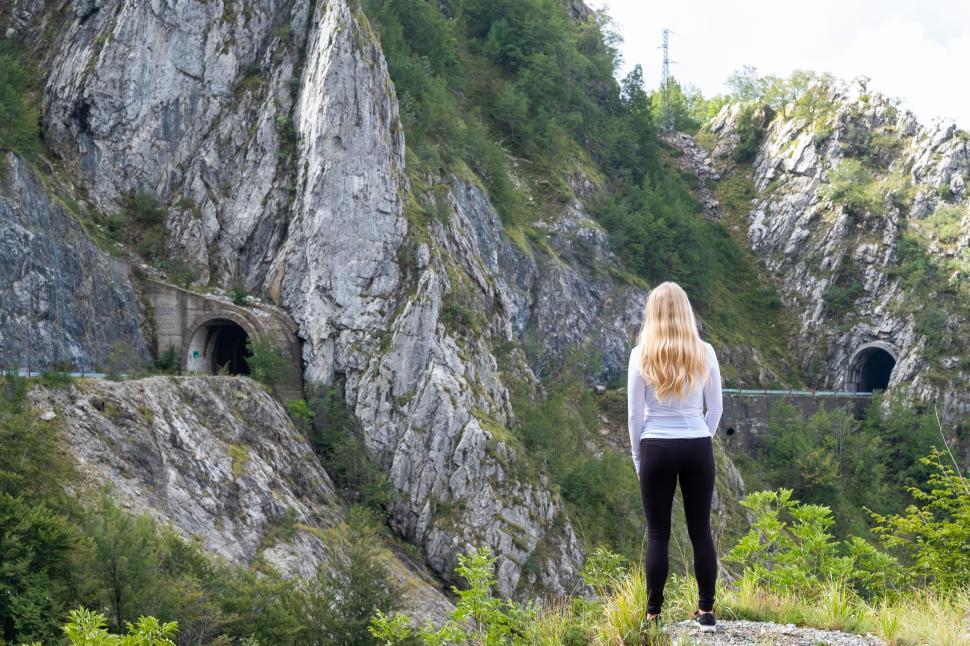 Free Image of Woman stands on rocky overlook near mountain tunnels 