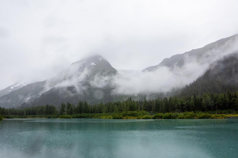 Free Image of Majestic mountains shrouded in mist reflect softly on calm lake 