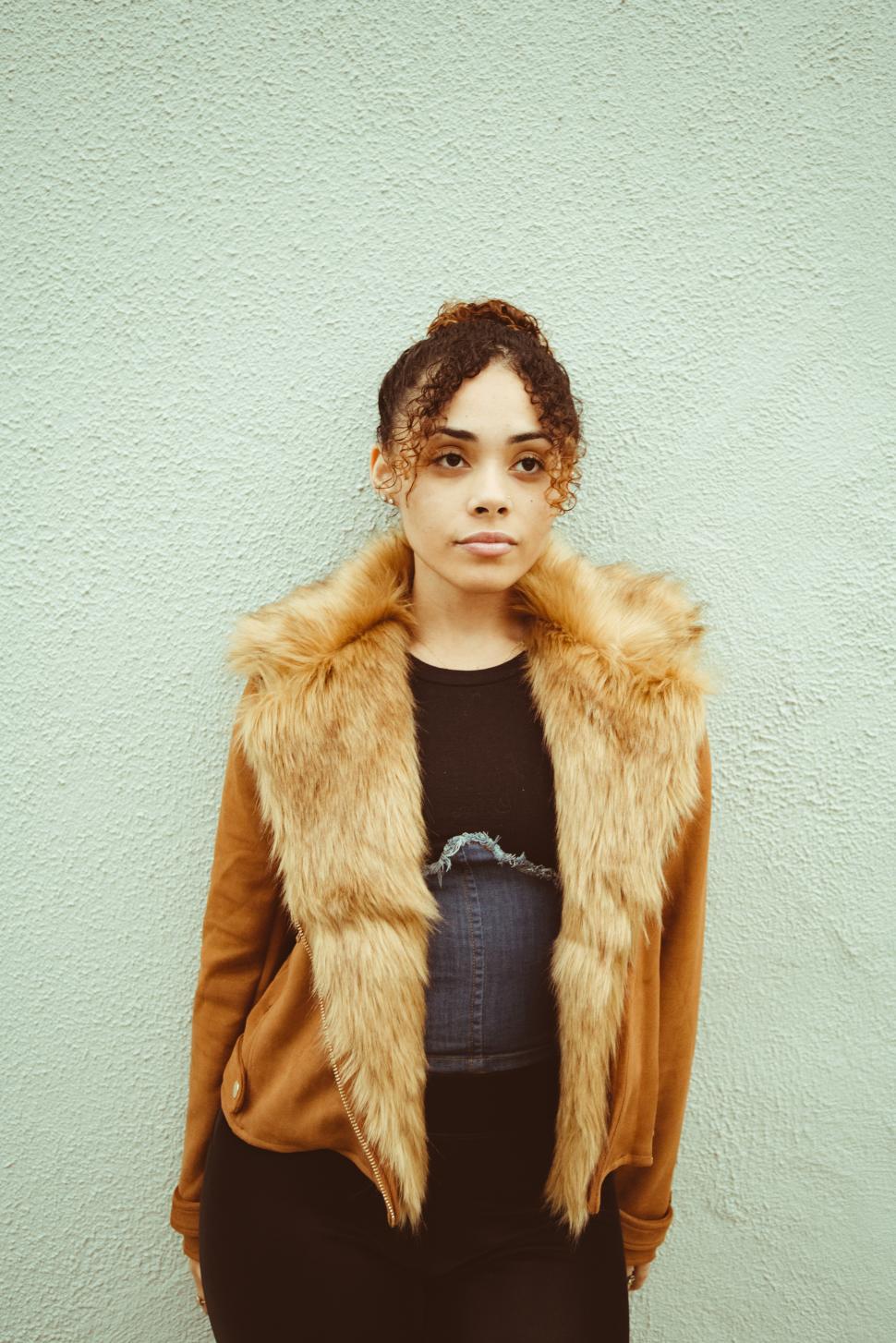 Free Image of Young woman in stylish fur coat stands against textured wall 
