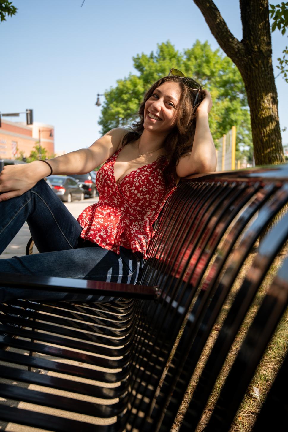 Free Image of Woman enjoying a sunny day on a park bench in a lively urban setting 