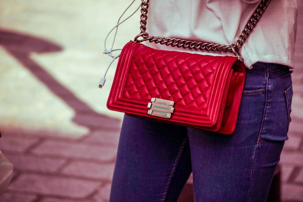 Free Image of Stylish woman showcases vibrant red handbag while walking through urban street 