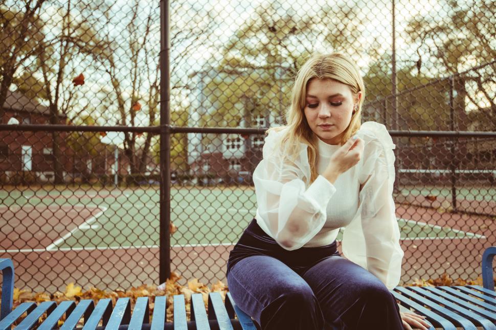 Free Image of Woman sitting on a bench at a tennis court during autumn 