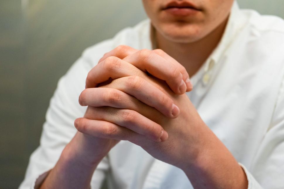 Free Image of Man sitting quietly with hands clasped in a thoughtful pose indoors 