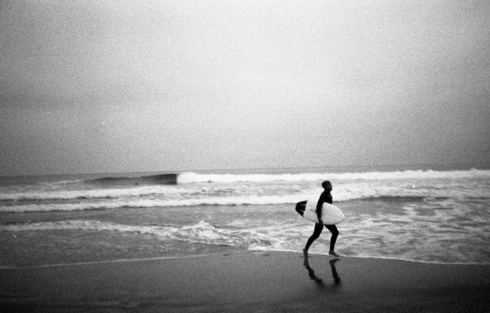 Free Image of Surfer walking along the shore on a cloudy day 