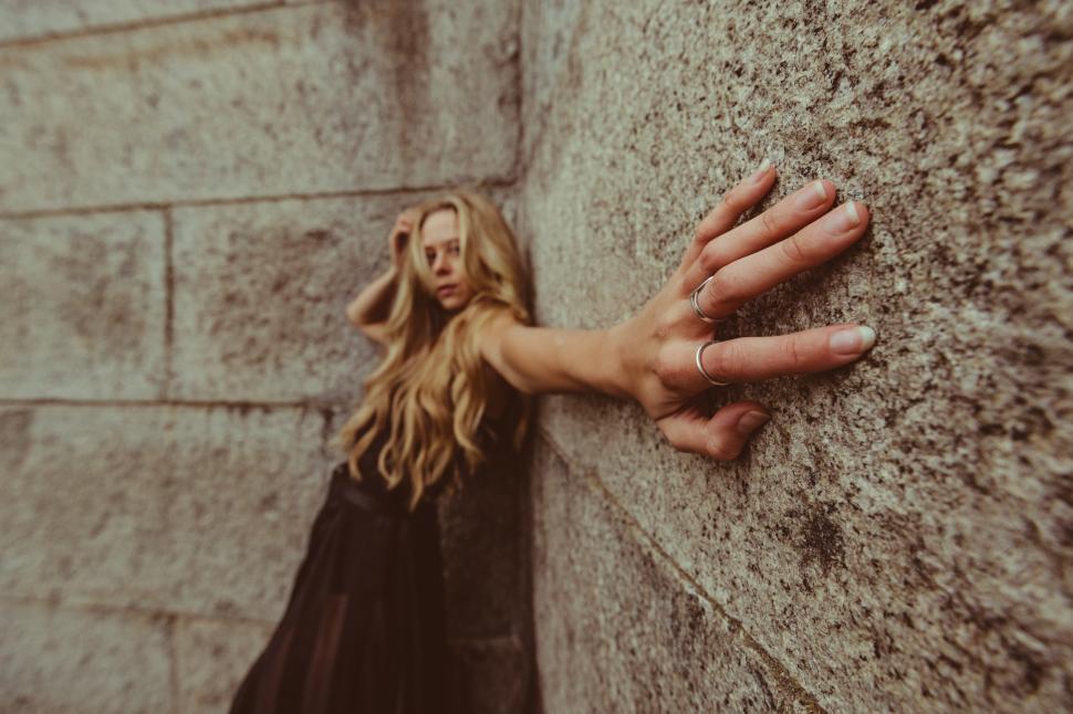 Free Image of Woman reaching out against a textured stone wall at sunset 