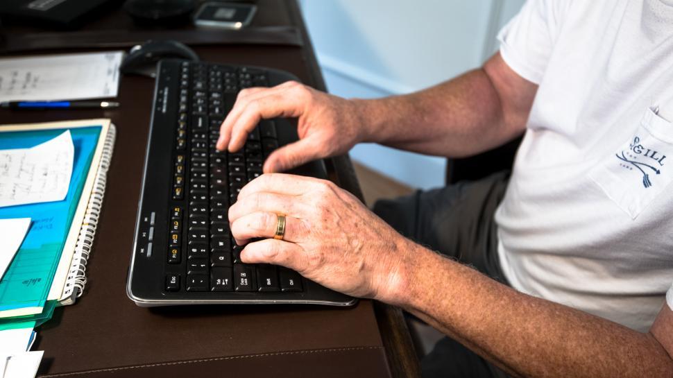 Free Image of Person typing on a keyboard at a wooden desk surrounded by office supplies 