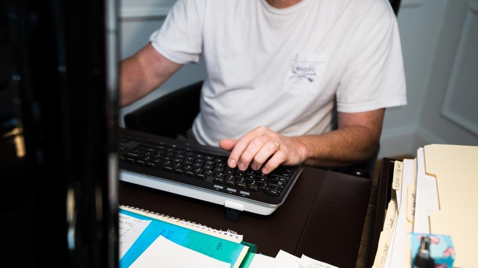 Free Image of Working on a computer in a home office while managing paperwork and files 