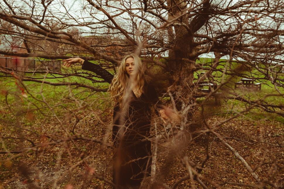 Free Image of Woman standing among tree branches in a peaceful outdoor setting 