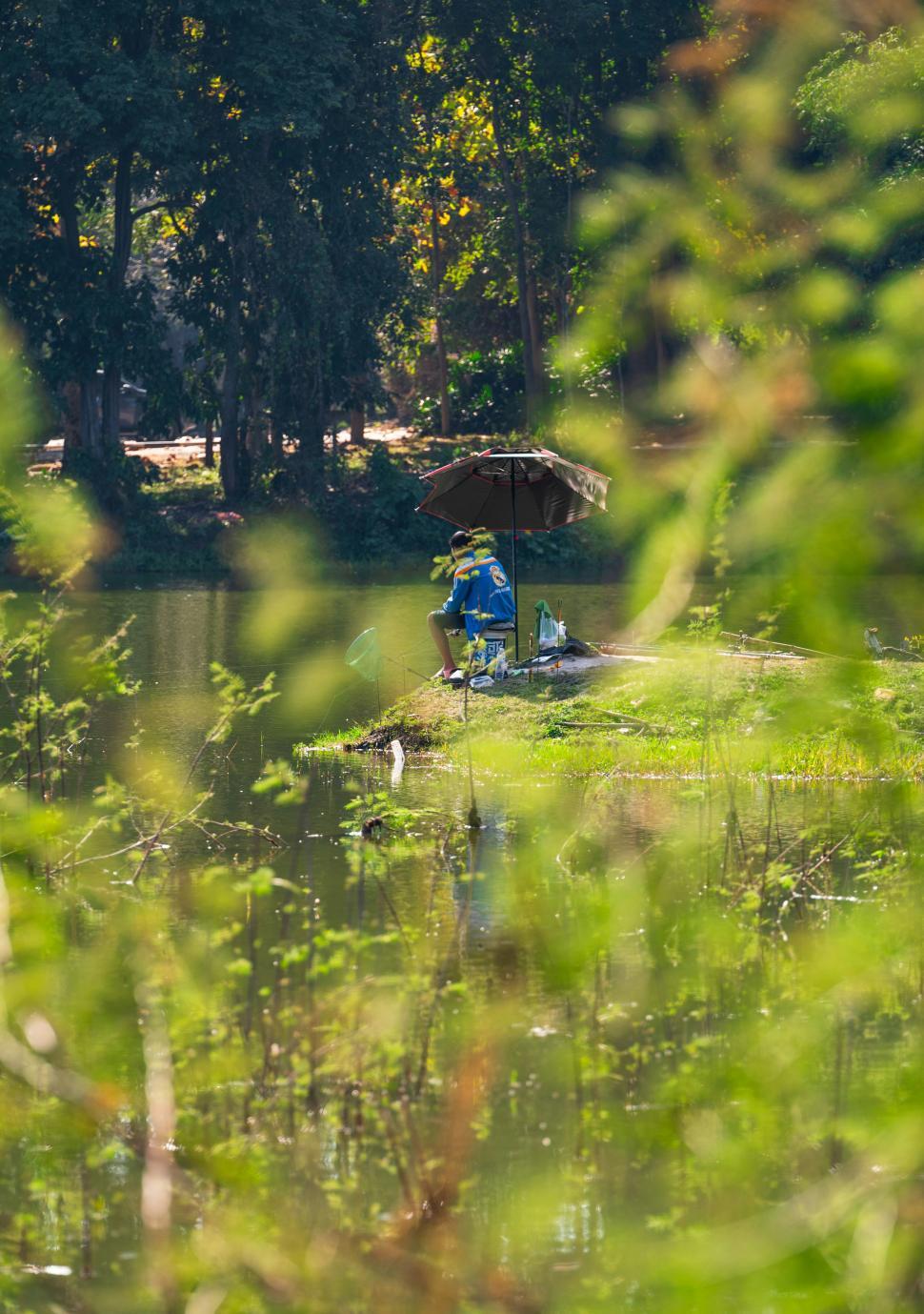 Free Image of Fisherman under an umbrella enjoying a sunny day by the lake 