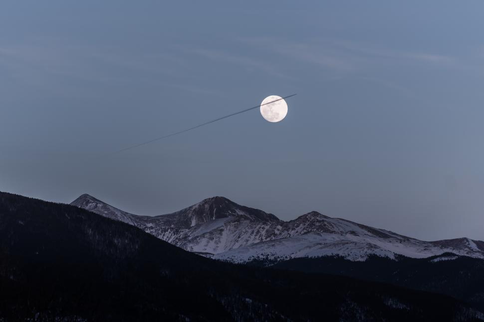 Free Image of Mountains illuminated by a full moon with a plane s contrail crossing the sky 