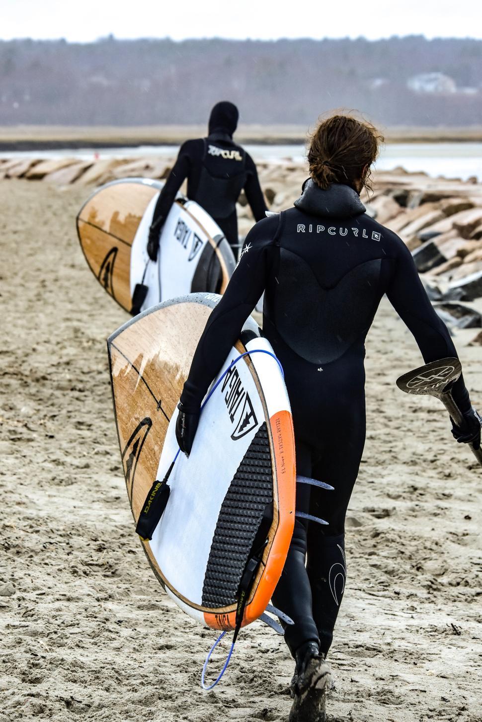 Free Image of Surfers prepare for a session on a sandy beach in cool weather near the shore 