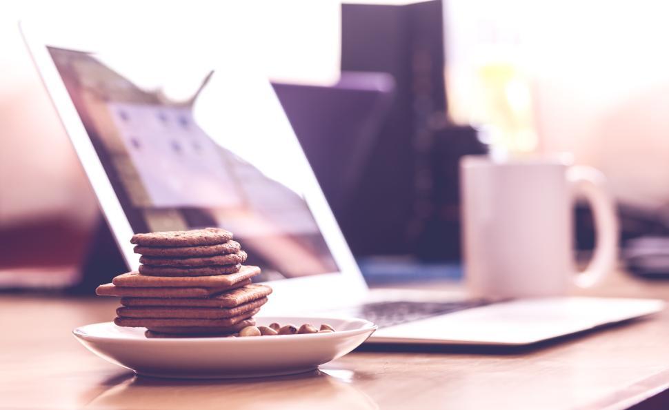 Free Image of Cookies on a plate next to a laptop at a workspace 