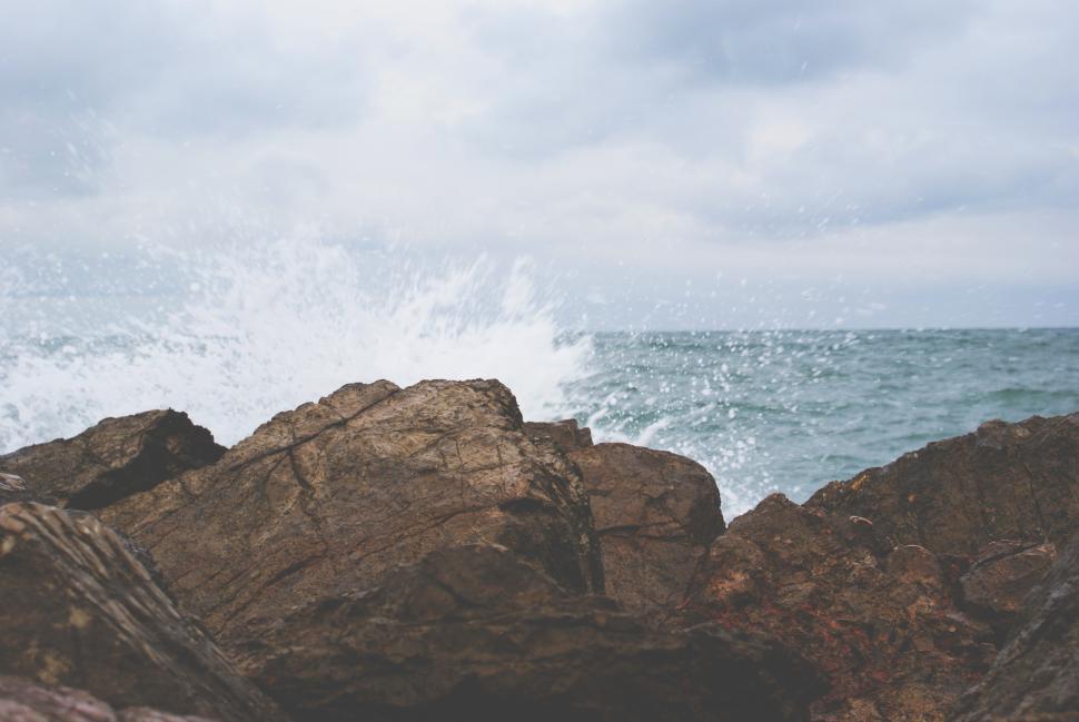 Free Image of Waves crashing against rocky shore under cloudy sky during morning light 