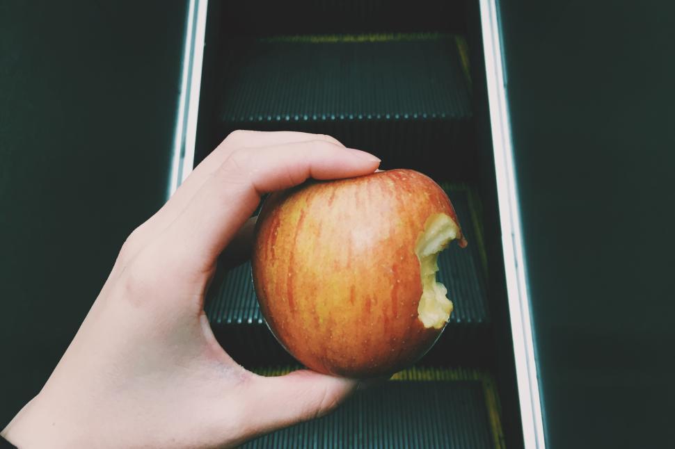 Free Image of Hand holding bitten apple on escalator step 